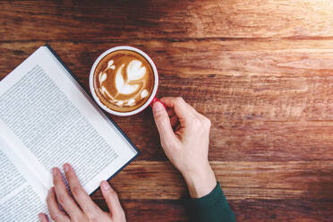 Cropped Image Of Woman Holding Coffee Cup While Reading Book On Table - EYF04406