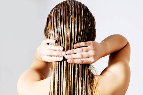 Rückansicht einer Frau, die Conditioner auf die Haare aufträgt, vor weißem Hintergrund - EYF04473