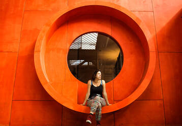 Full Length Of Woman Sitting On Window Of Orange Building - EYF04546