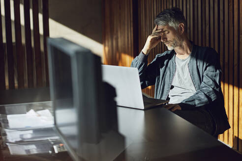 Ein lässiger Geschäftsmann sitzt in seinem nachhaltigen Büro, in der Hand - MCF00639
