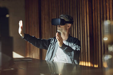 Casual businessman sitting in his sustainable office, looking through VR glasses - MCF00643