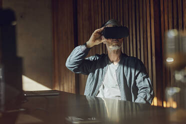 Casual businessman sitting in his sustainable office, looking through VR glasses - MCF00644