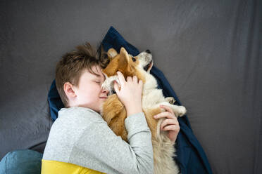 Portrait of boy lying on bed cuddling his dog - VPIF02318