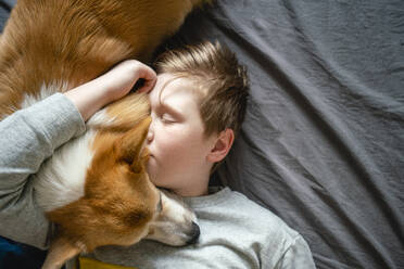 Portrait of boy lying on bed cuddling his dog - VPIF02338