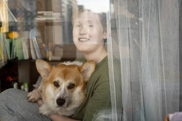 Portrait of smiling boy and his dog looking out of window - VPIF02339