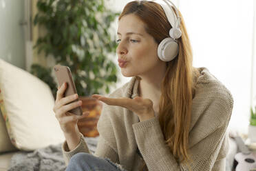 Young woman with headphones and smartphone chatting at home - AFVF05993