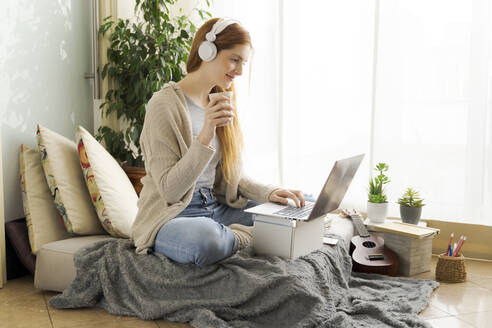 Young woman wearing headphones and using laptop at home - AFVF05996