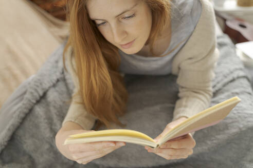 Junge Frau liegt auf einer Decke und liest in einem Notizbuch - AFVF06005