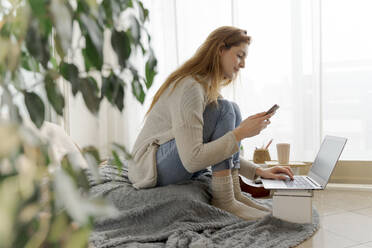 Junge Frau nutzt Smartphone und Laptop zu Hause - AFVF06009