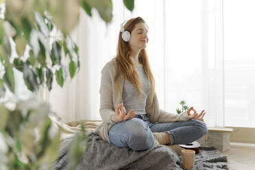 Junge Frau mit Kopfhörern, die zu Hause Yoga übt - AFVF06011