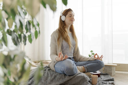 Young woman wearing headphones and practicing yoga at home - AFVF06011