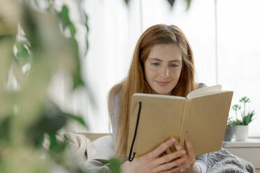 Junge Frau liest zu Hause in einem Notebook - AFVF06018