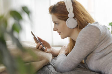 Young woman wearing headphones and using smartphone at home - AFVF06027