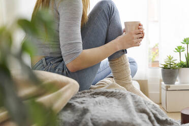 Low section of young woman with coffee mug at home - AFVF06028