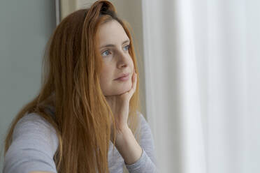 Porträt einer ernsten jungen Frau, die aus dem Fenster schaut - AFVF06030