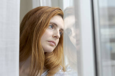 Porträt einer ernsten jungen Frau, die aus dem Fenster schaut, lizenzfreies Stockfoto