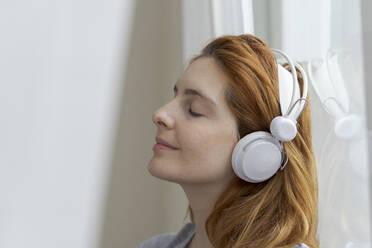 Young woman listening to music with headphones at the window - AFVF06033