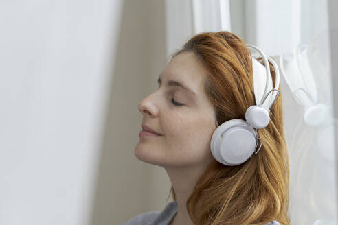 Junge Frau, die mit Kopfhörern am Fenster Musik hört - AFVF06033