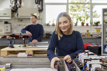 Porträt einer lächelnden Elektrikerin bei der Arbeit an einem Schaltkreis in einer Werkstatt - ZEDF03226