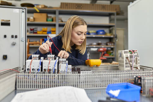 Female electrician working with voltmeter on circuitry in workshop - ZEDF03230