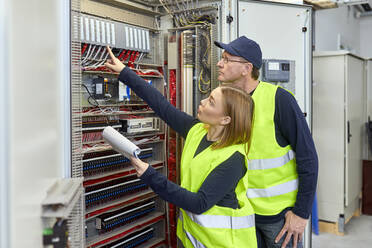 Two electricians with plan looking at fuse box - ZEDF03236