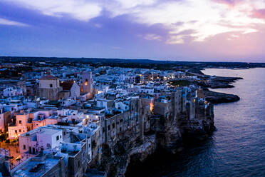 Italien, Polignano a Mare, Blick aus dem Hubschrauber auf die Klippen und Gebäude der Küstenstadt in der Abenddämmerung - AMF08002