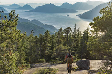 Rear View Of Man Riding Bicycle On Mountain Against Sky - EYF04587