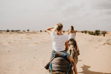 Rückansicht von Frauen reiten Kamele in der Wüste - EYF04786