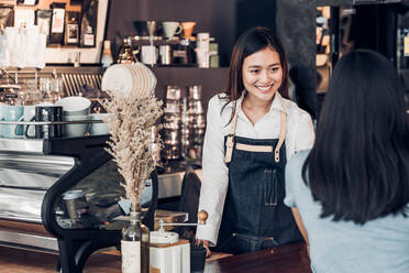 Smiling Owner Talking To Customer While Standing At Counter In Cafe - EYF04827