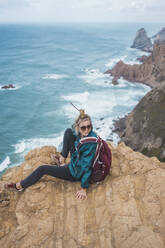 Portugal, Bezirk Lissabon, Sintra, Weiblicher Rucksacktourist am Rande der Klippe Cabo da Roca sitzend - FVSF00127