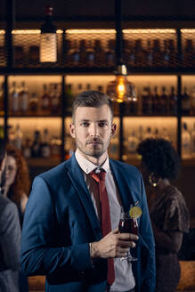 Porträt eines ernsten jungen Mannes, der in einer Bar einen Cocktail trinkt - ZEDF03288