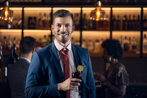 Porträt eines glücklichen jungen Mannes, der in einer Bar einen Cocktail trinkt - ZEDF03289