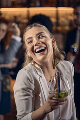 Portrait of a happy young woman having a cocktail in a bar - ZEDF03294