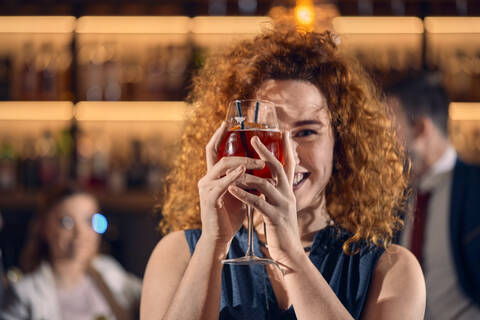 Porträt einer glücklichen jungen Frau, die ein Cocktailglas in einer Bar hält, lizenzfreies Stockfoto