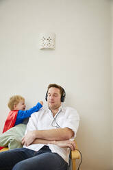 Boy wearing superman costume and annoying father while listeining to music with headphones - FSF01024