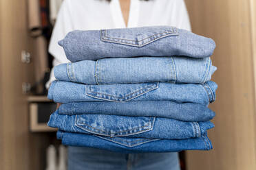 Woman holding stack of blue jeans - FMOF00967