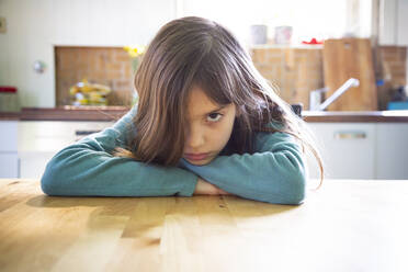Annoyed girl sitting in kitchen, leaning on table - LVF08806