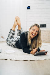 Portrait of laughing woman lying on the floor using mini tablet - MPPF00786