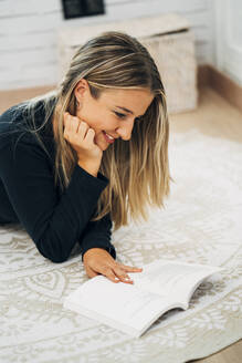 Woman lying on the floor at home reading a book - MPPF00787