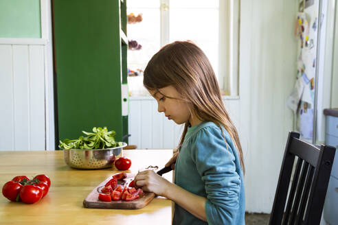 Girl cutting tomatoes on chopping board in kitchen - LVF08808