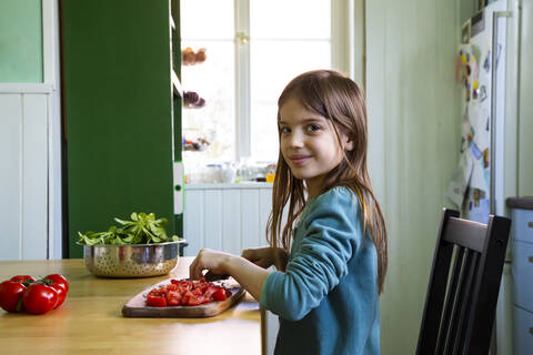 Lächelndes Mädchen schneidet Tomaten auf einem Schneidebrett in der Küche, lizenzfreies Stockfoto