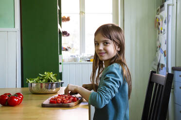 Smiling girl cutting tomatoes on chopping board in kitchen - LVF08809