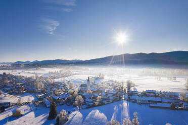 Deutschland, Bayern, Reichersbeuern, Drone view of sun shining over snow-covered village - SIEF09759