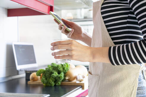 Young woman preparing healthy meal, using smartphone - AFVF06034