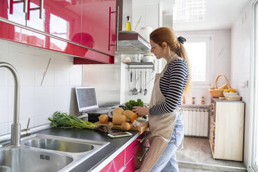 Young woman havig a video chat, while cooking a healthy meal - AFVF06040