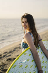 Porträt einer lächelnden jungen Frau mit Surfbrett am Strand, Almeria, Spanien - MPPF00821