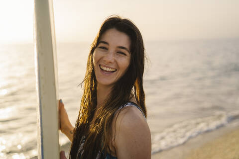 Porträt einer lachenden jungen Frau mit Surfbrett am Strand, Almeria, Spanien, lizenzfreies Stockfoto