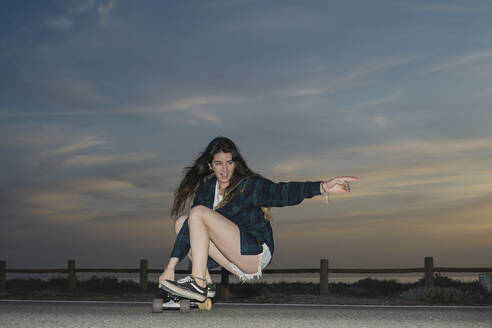 Young woman skateboarding on asphalt road at dusk, Almeria, Spain - MPPF00833