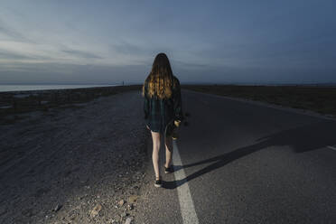 Rückenansicht einer jungen Frau mit Skateboard auf einer asphaltierten Straße, Almeria, Spanien - MPPF00834