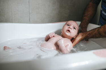 Baby girl bathing, holding by father's hands - KIJF02968